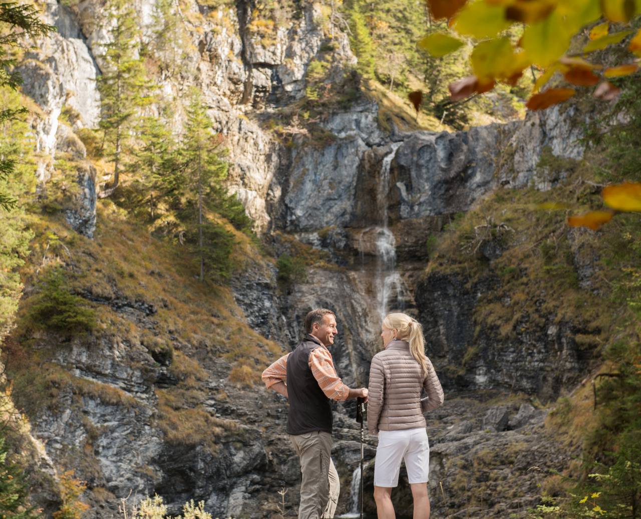 Mann und Frau vor einem kleinen Wasserfall in den Bergen beim Wandern im Herbst