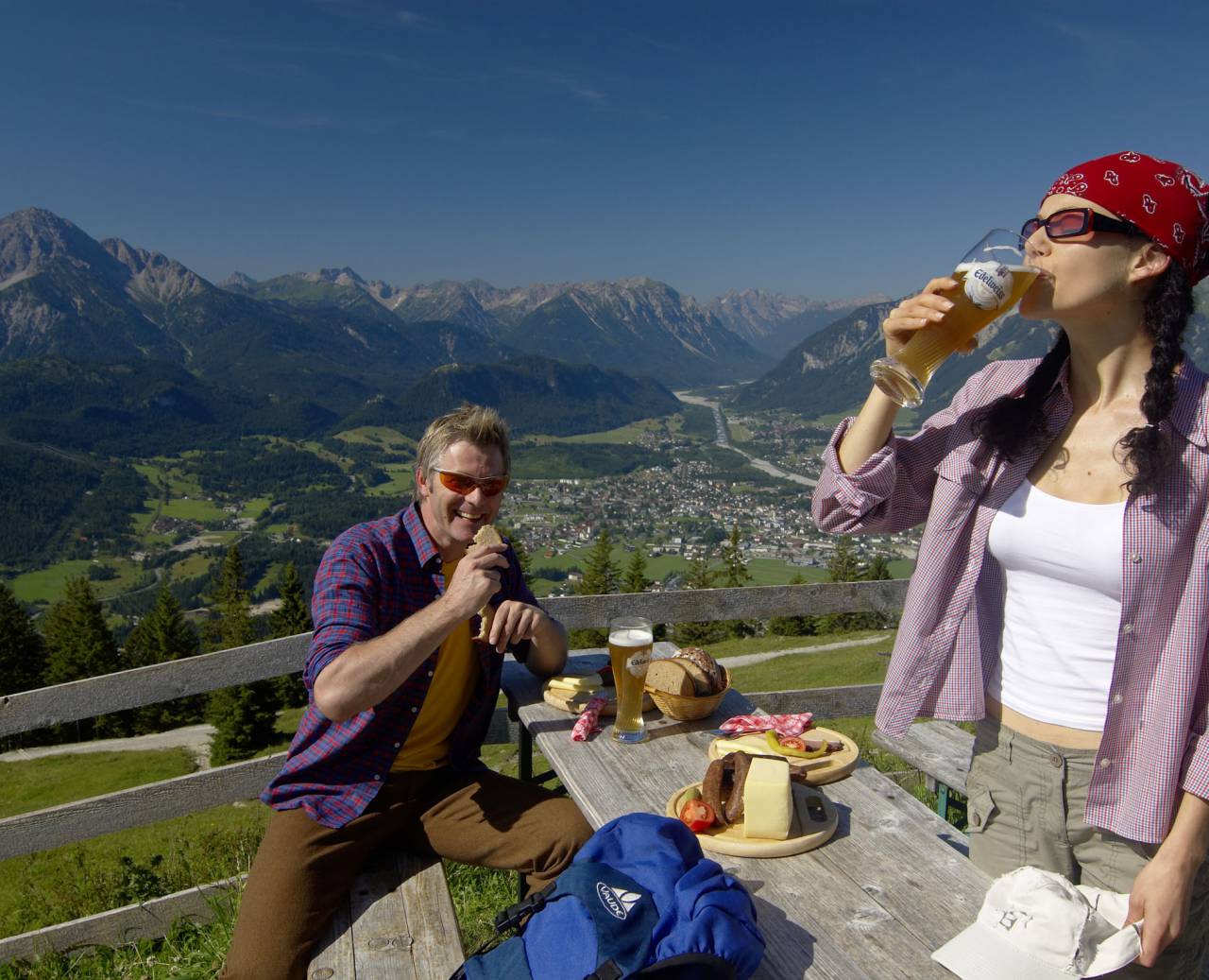 Couple having a snack in the mountains with sausage, cheese and a cold beer