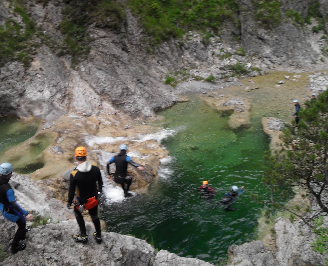 Canyoning group in wetsuits jumping into clear green water among rocky cliffs