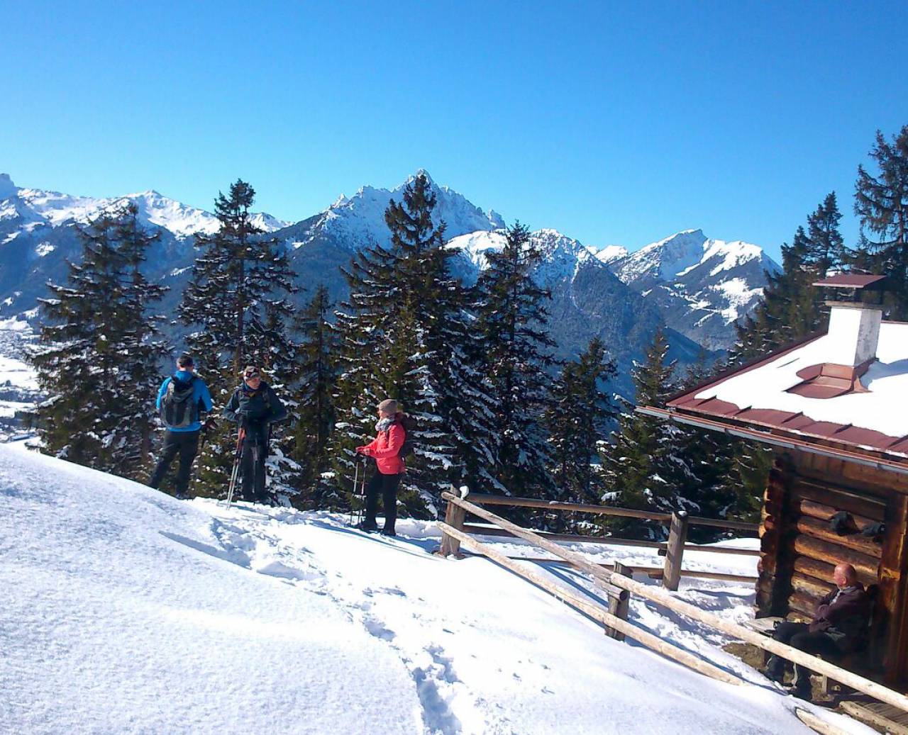 Sneeuwschoenwandelaars bij een blokhut met panoramisch uitzicht op besneeuwde bergen
