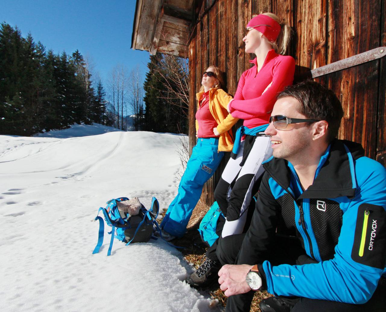 Vakantiegangers genieten van de winterzon bij een besneeuwde hut