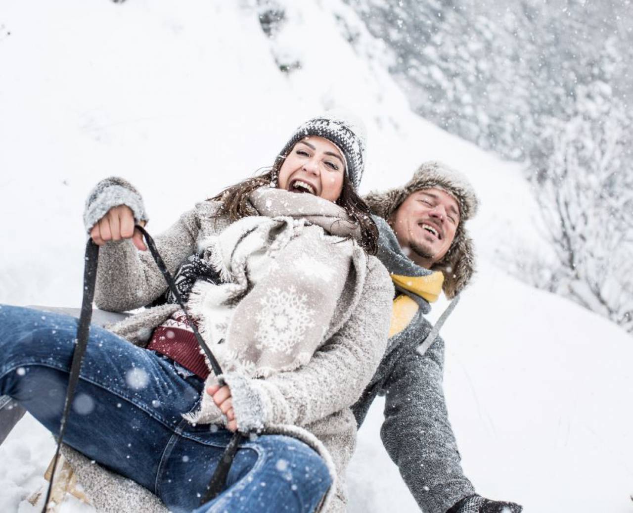 Couple tobogganing in the forest during snowfall