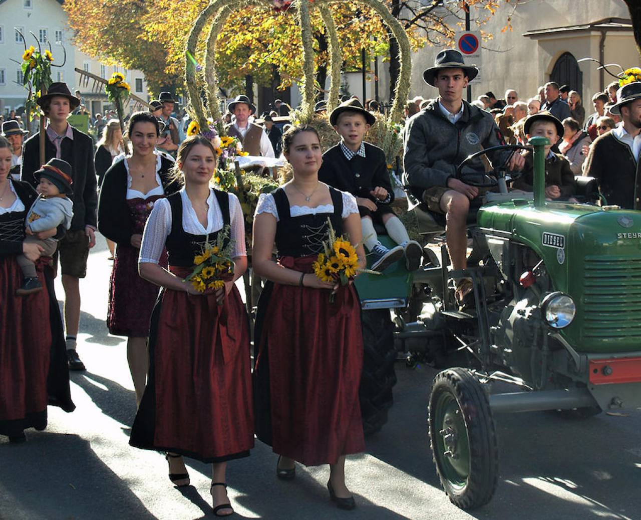 Parade with dirndls, traditional dress and a decorated tractor in the sun