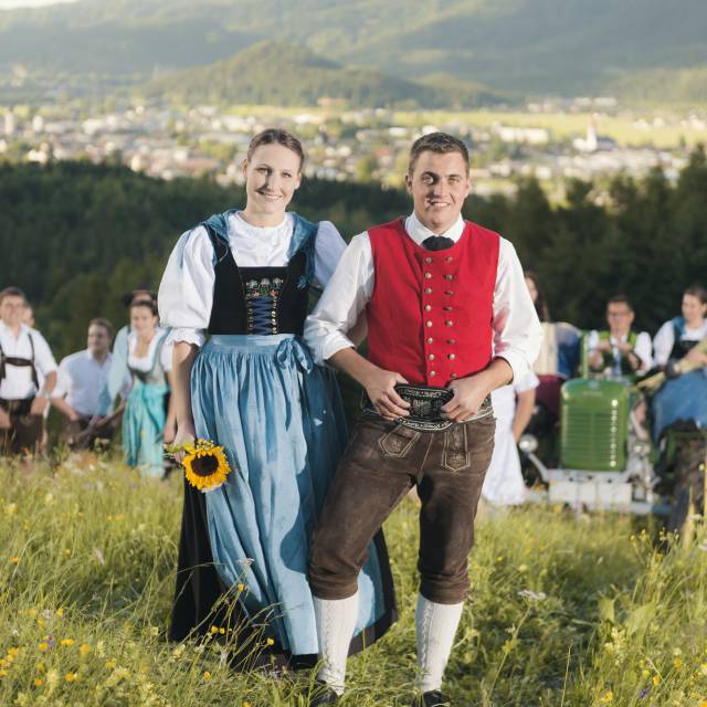 Stel in klederdracht poseert op een bloeiende alpenweide met uitzicht op het dal