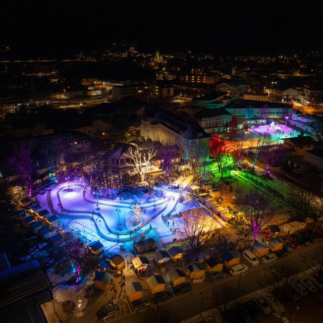 Bunte Lichtshow auf der Eisbahn bei Nacht in Reutte, Tirol, mit Blick auf die Stadt