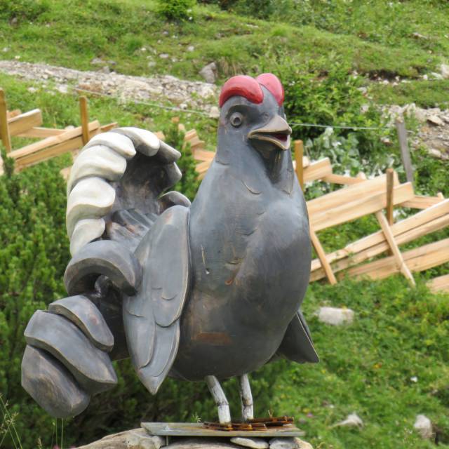 Sculpture of a rooster made of wood and metal on an alpine meadow