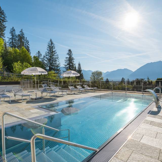 Buitenzwembad met zonneterras, ligstoelen en parasols voor het hotel – omgeven door natuur en bergen