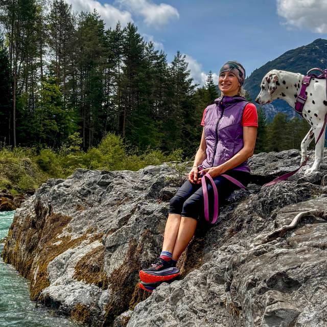 Frau mit Hund macht eine Pause am türkisfarbenen Lechfluß