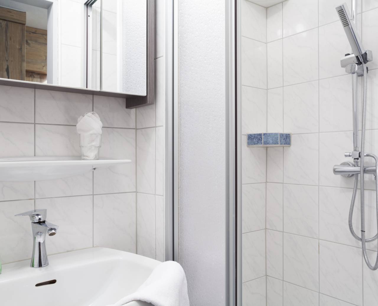 Weiß gefliestes Badezimmer mit Dusche, Waschbecken und Spiegelkasten