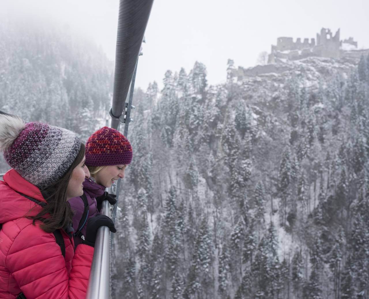 Women on the suspension bridge highline179 in winter with a view of the snow-covered ruin Ehrenberg