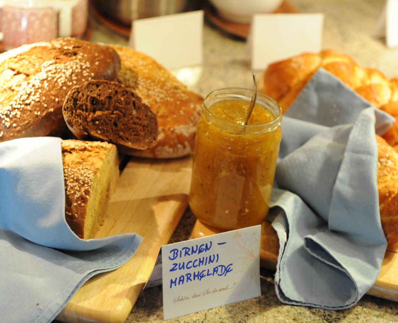 Frisches Weiß- und Schwarzbrot auf Schneidbrettern mit Birnen-Zucchini-Marmelade im Glas