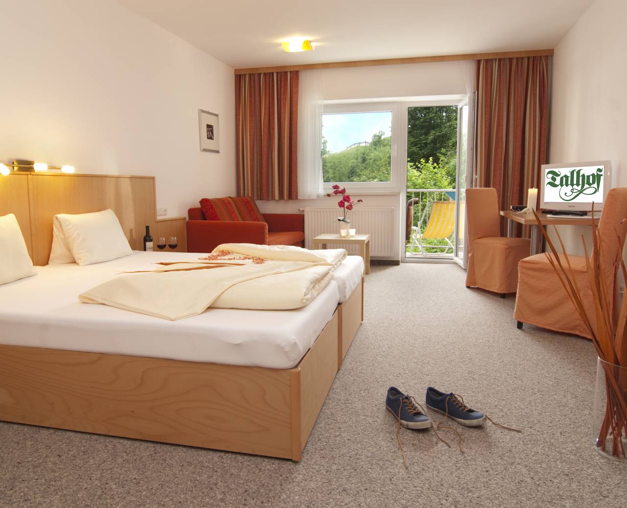Hotelzimmer mit Doppelbett, Sitzgarnitur und Balkon mit Ausblick in die Natur