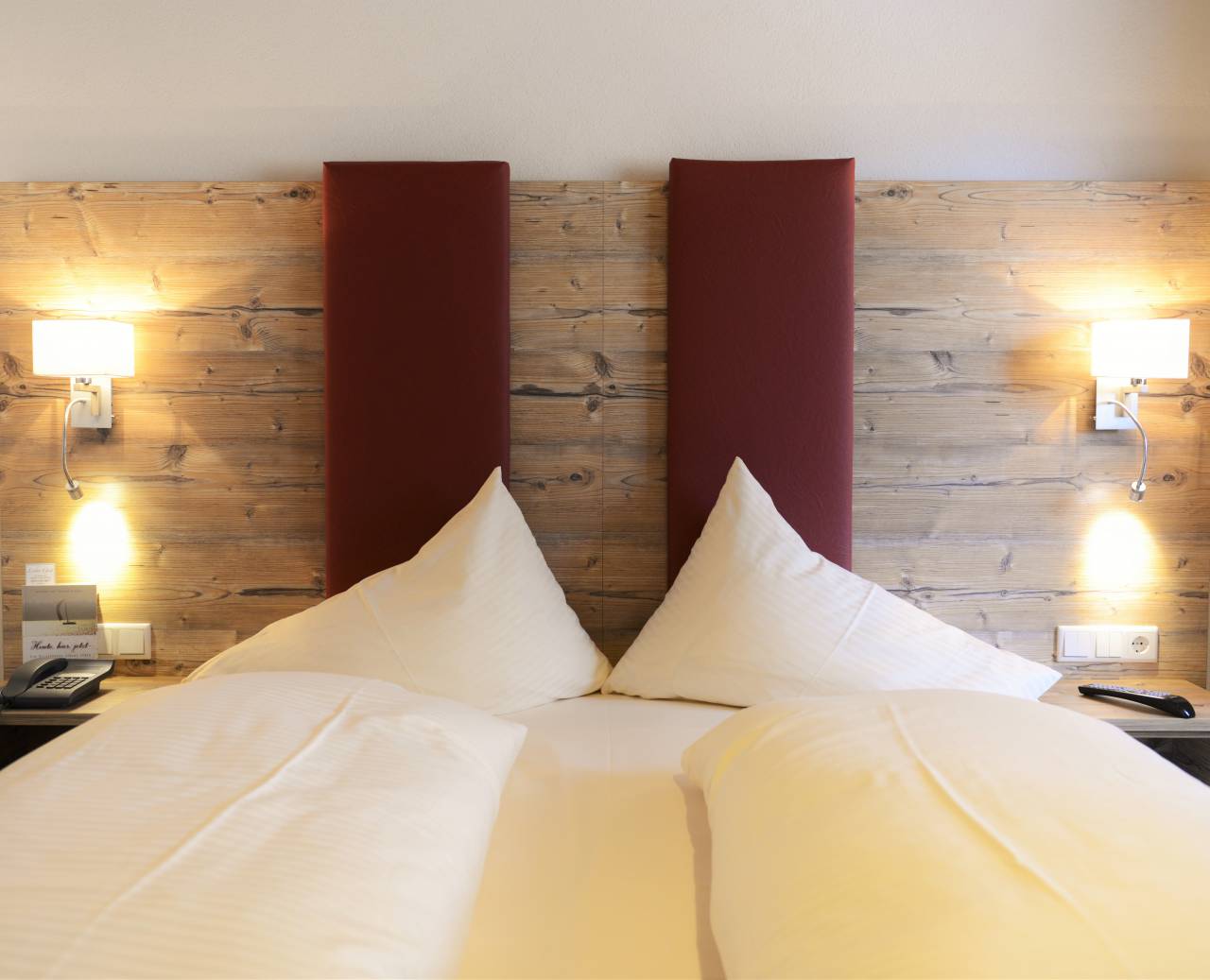 Großes Doppelbett mit gepolstertem Kopfteil in Holzoptik und Nachtischlampen