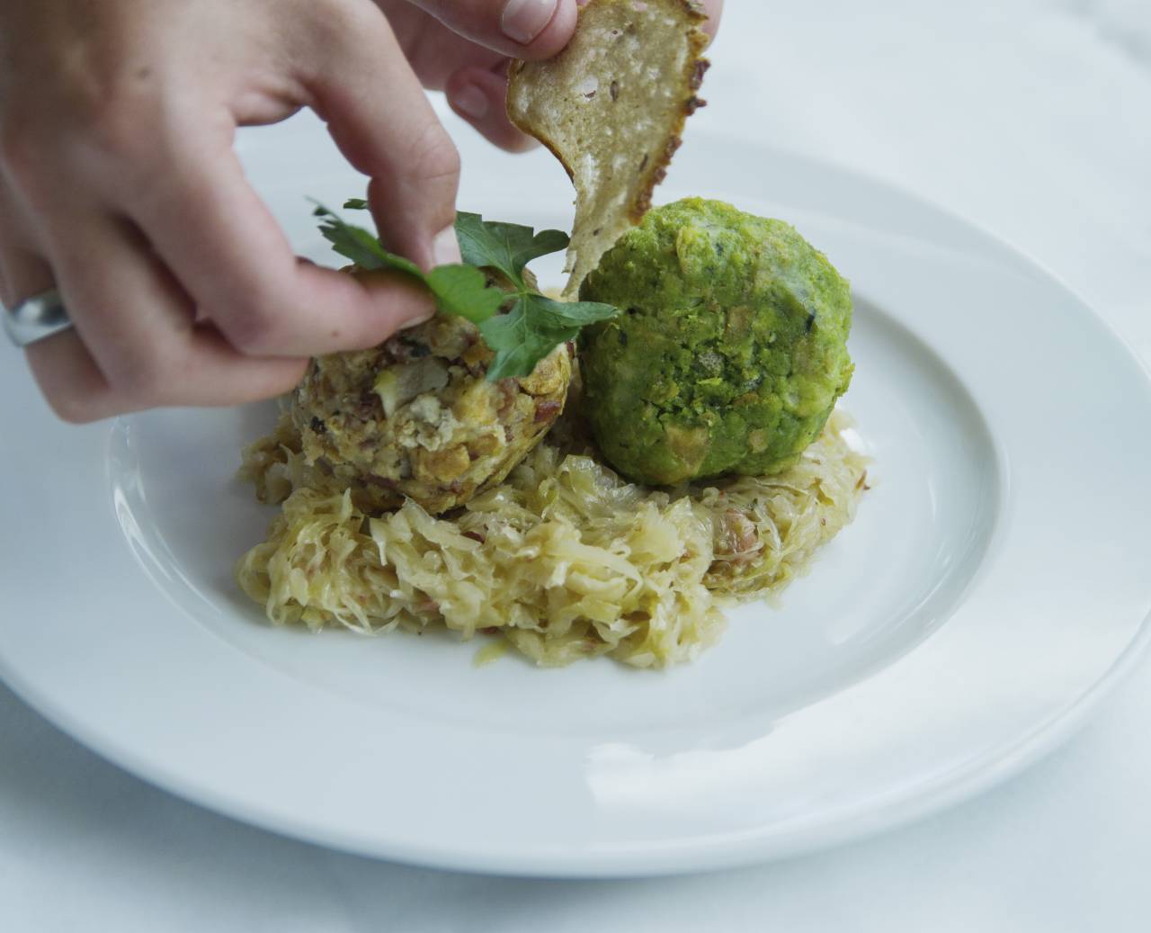 Köchin garniert Speckknödel und Spinatknödel auf einem Sauerkrautbett