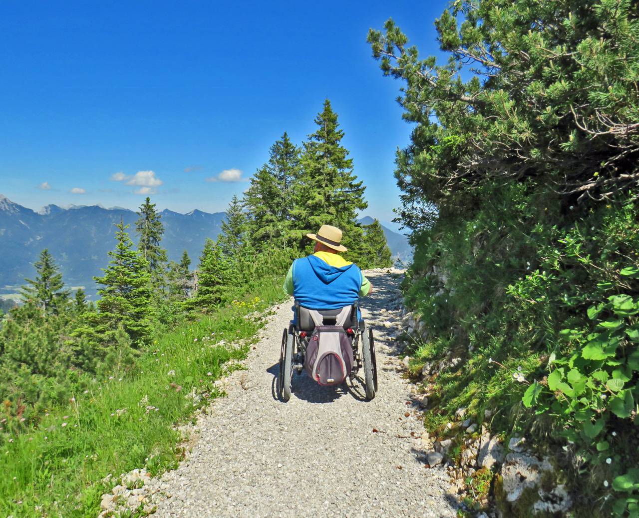 Rollstuhlfahrer auf einem Waldweg in der Natur mit Blick auf das Tal und die Berge im Sommer